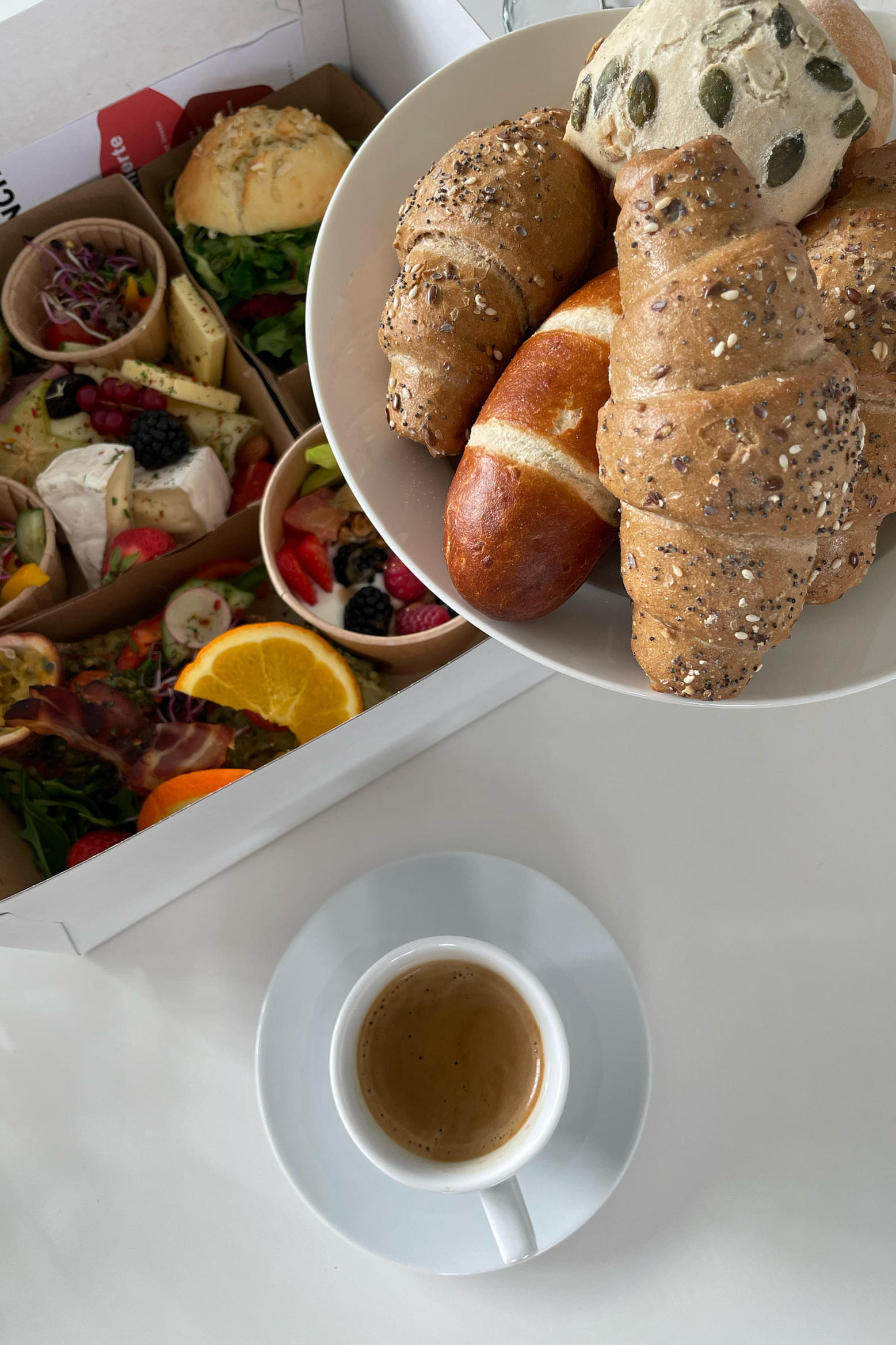 Ein Teller mit verschiedenen Brötchen wird über einer Frühstücksbox mit Obst und Aufschnitt gehalten.